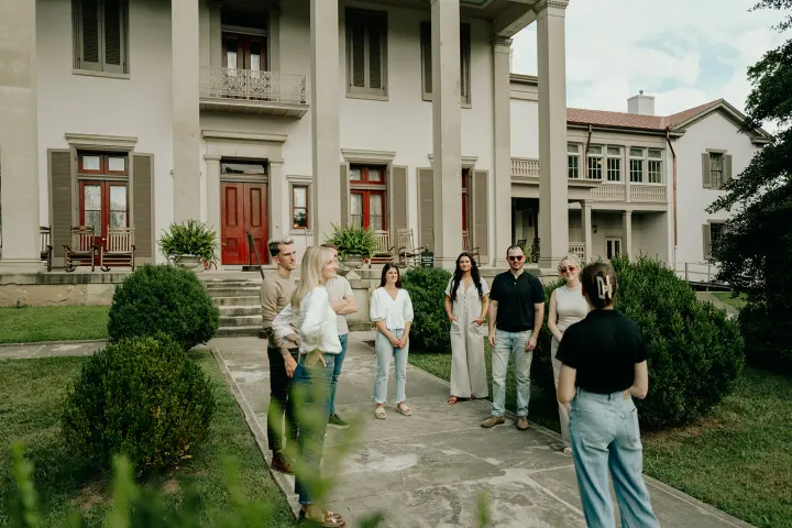 Group of people standing on a path in front of a large building with columns.