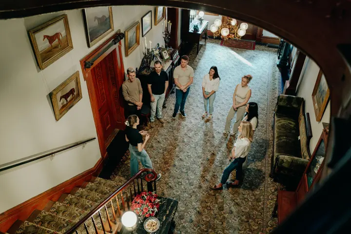 Group of people standing in a spacious carpeted hallway with paintings on the walls.