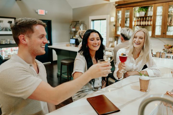 Three people smiling, toasting with drinks at a bar counter.
