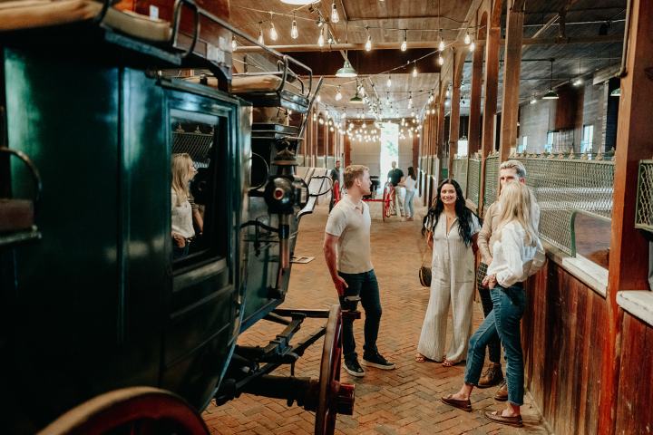Four people chatting in a rustic barn setting with a vintage carriage.