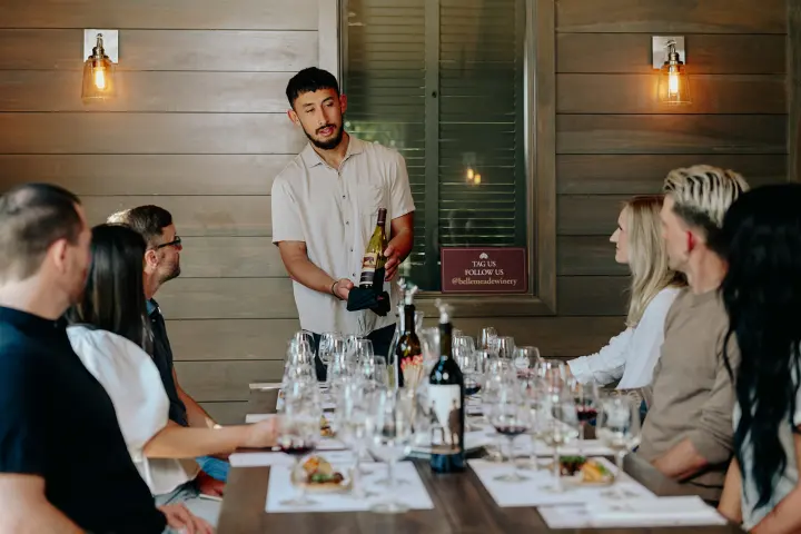 Man presenting wine to seated group at a tasting event.