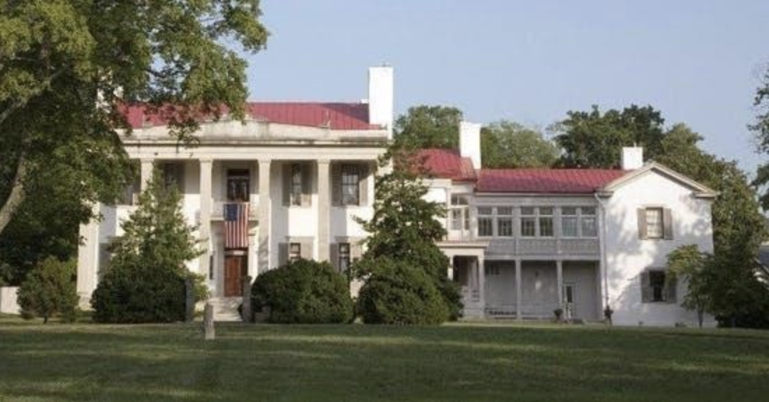 a large brick building with grass in front of a house with Belle Meade in the background