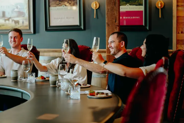 Four people raising wine glasses at a dining table, smiling.