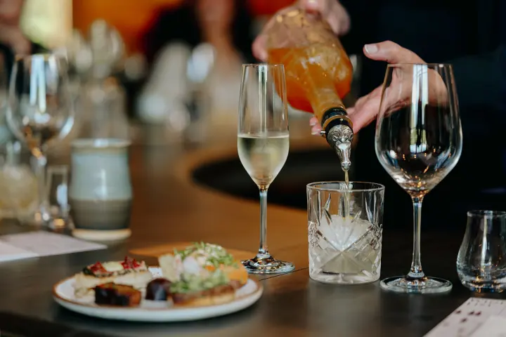 Bartender pouring drinks with a plate of appetizers and empty glasses on the table.