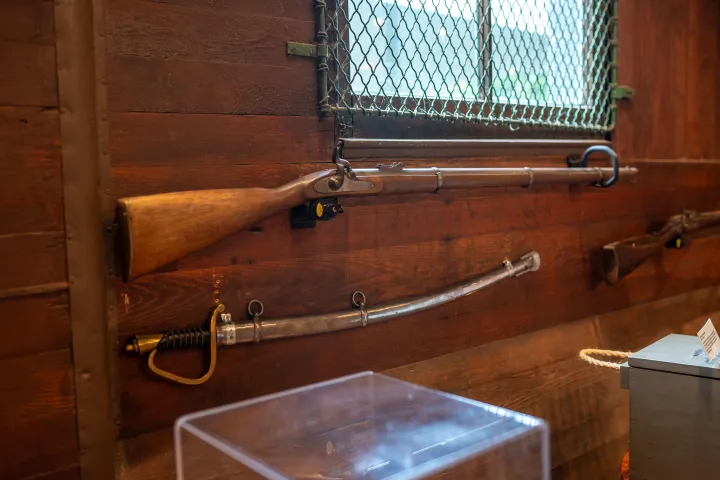 Old rifle and sword displayed on a wooden wall with a barred window.