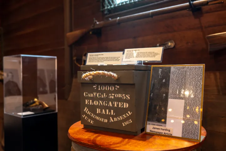 Museum display of historic ammo box and newspaper article with rifles in the background.