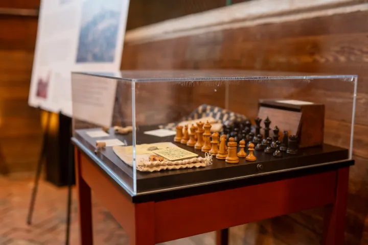 Chess set displayed in a glass case with wooden pieces on a table.