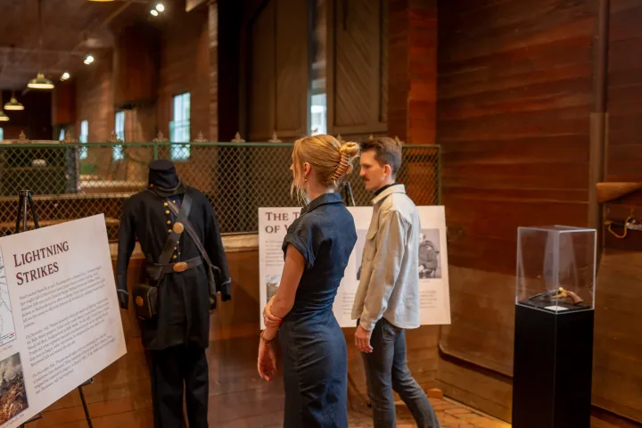 Two people view a museum exhibit featuring a Civil War uniform and informational displays.
