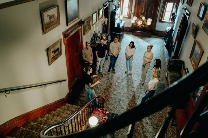 Group of people standing in a hallway with staircase, viewed from above.