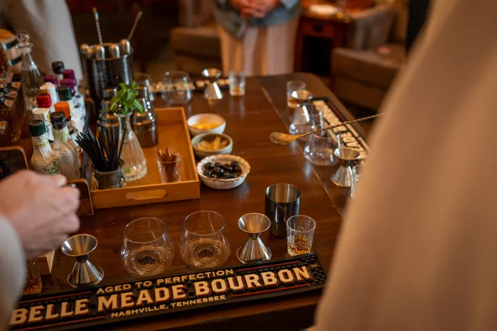 Bar setup with bourbon, glasses, and mixers on a wooden table.