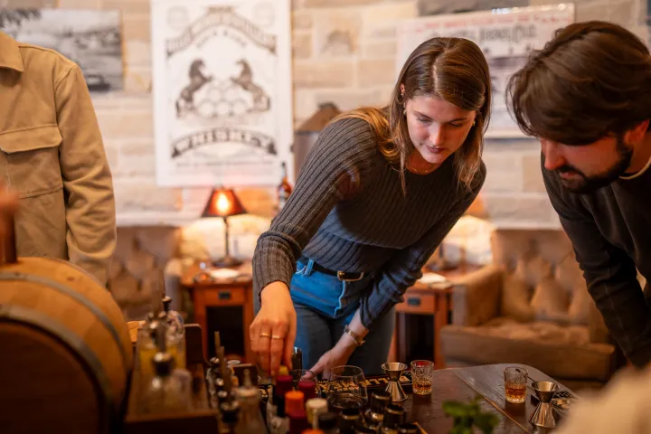 Three people gathered around a table with various bottles and glasses in a cozy room.