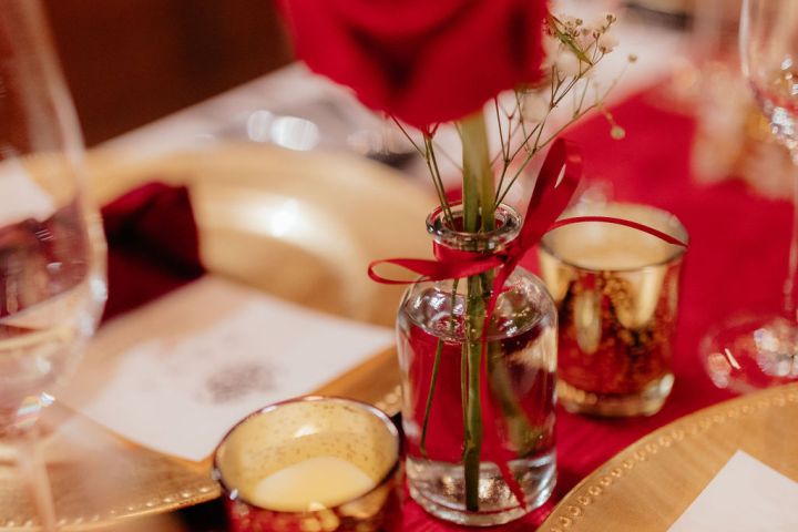 Table setting with red rose in glass vase, gold plate, and candles.
