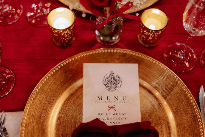 Elegant table setting with gold plates, red roses, menu, and candles.