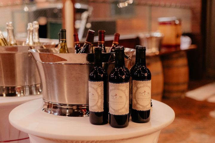 Wine bottles and ice buckets on a draped table at an indoor event space.