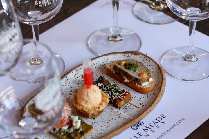 Four empty wine glasses and gourmet appetizers on a table mat with Belle Meade Winery logo.