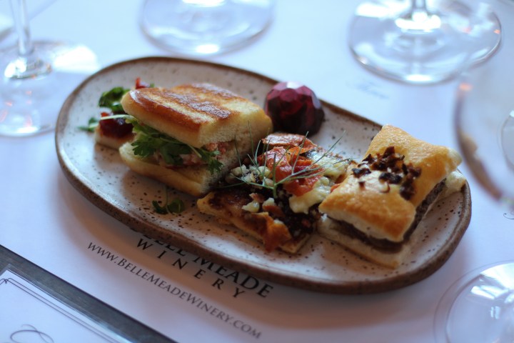 Assorted gourmet appetizers on a ceramic plate beside wine glasses.