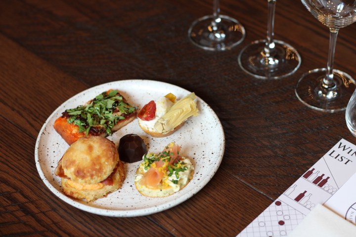 Plate of assorted appetizers on a wooden table with wine glasses.