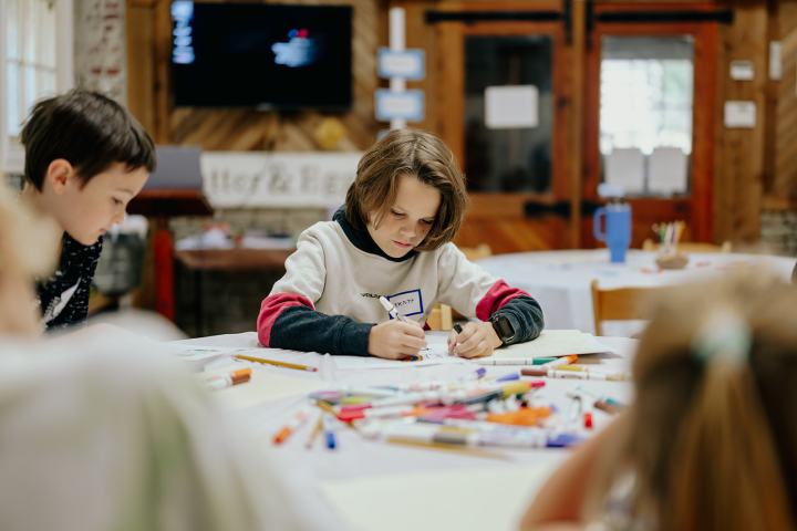Children focused on drawing at a table with art supplies in a cozy room.