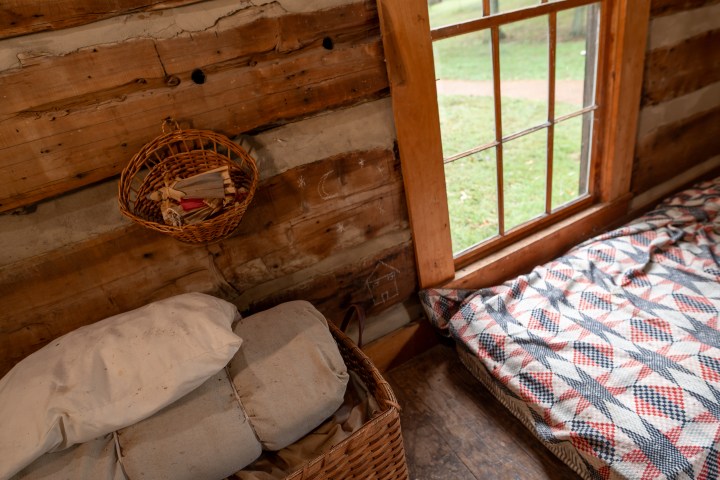 Rustic cabin interior with bed and wicker basket by window.